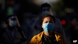 FILE - A girl wearing a face mask waits with dozens of others to get a coronavirus test at the National Stadium in Phnom Penh, Cambodia, Tuesday, Dec. 8, 2020.