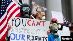 Seorang pedemo mengenakan masker memegang poster di tengah demo di gedung Capitol, Olympia, menentang perpanjangan perintah tinggal di rumah untuk meredam penularan virus corona (Covid-19), Washington, 19 April 2020. (Foto: Reuters)