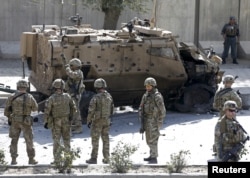 FILE - NATO soldiers stand near a damaged NATO military vehicle at the site of a suicide car bomb blast in Kabul, Afghanistan, Oct. 11, 2015.
