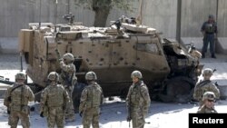 FILE - NATO soldiers stand near a damaged NATO military vehicle at the site of a suicide car bomb blast in Kabul, Afghanistan, Oct. 11, 2015. 