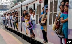 FILE - Commuters hang by doors of a crowded local train in Mumbai, India, July 8, 2014.