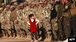 A girl stands in front of fighters from the Syrian Democratic Forces at the funeral of a fellow fighter killed in Hajin during battles against the Islamic State group, in the Kurdish-controlled city of Qamishly in northeastern Syria, Dec. 3, 2018. 