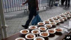 FILE - A man walks past served meals made with "wasted" produce deemed unsuitable by food stores because of their appearance, during an event against food waste in Athens, Greece, Oct. 11, 2015. 