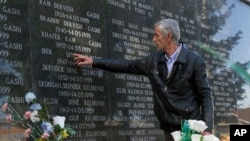 FILE - A survivor of the Cuska massacre points out the names of family members as he visits a cemetery in the village of Cuska, Kosovo, on Feb. 11, 2014.