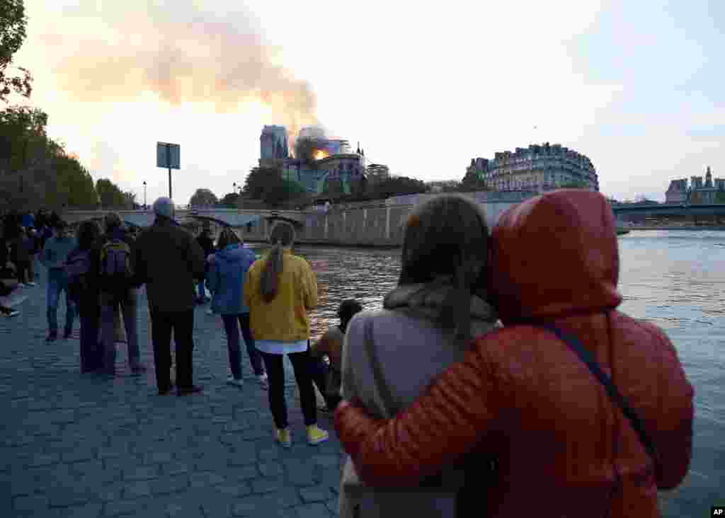 People watch as flames and smoke rise from Notre Dame cathedral as it burns in Paris, Monday, April 15, 2019. 