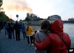 People watch as flames and smoke rise from Notre Dame cathedral as it burns in Paris, Monday, April 15, 2019.