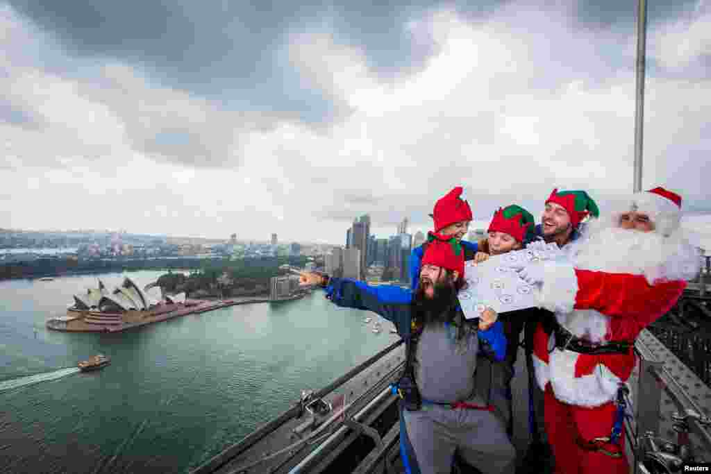 Lima orang memakai kostum Sinterklas bersama para perinya berdiri di atas jembatan Sydney Harbour di Sydney, Australia.
