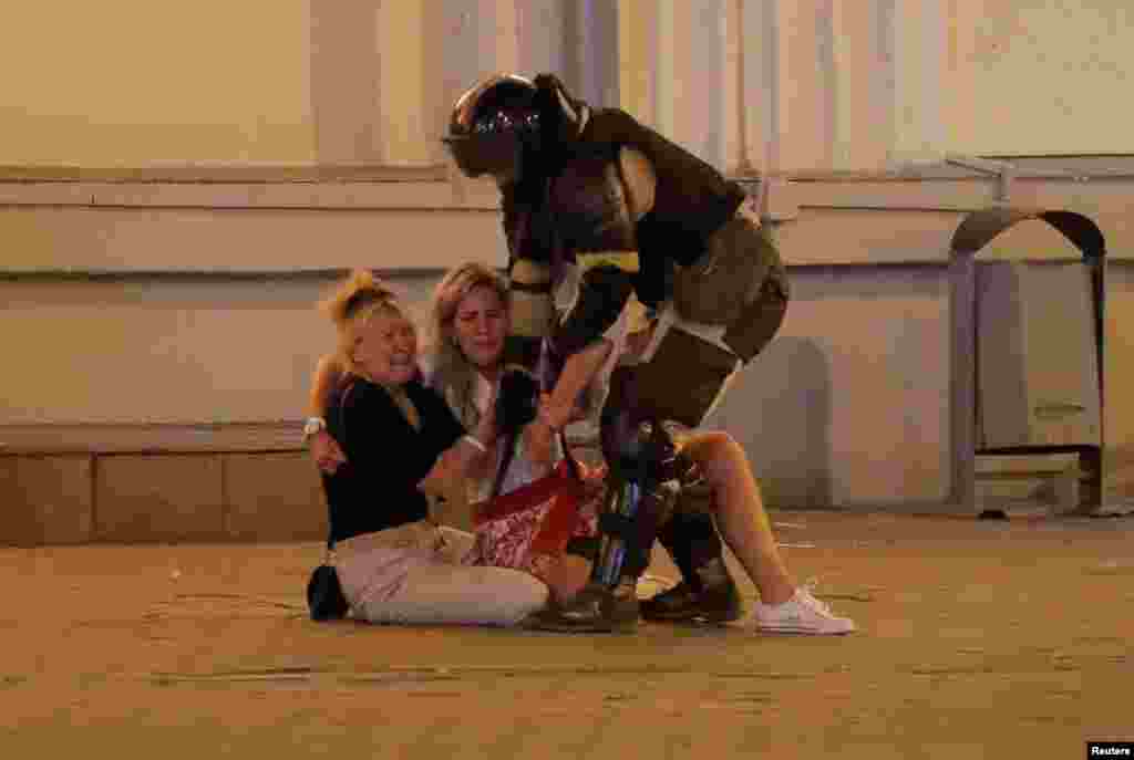 A law enforcement officer approaches women, who react while sitting on the pavement during a rally of opposition supporters following the presidential election in Minsk, Belarus, Aug. 10, 2020.