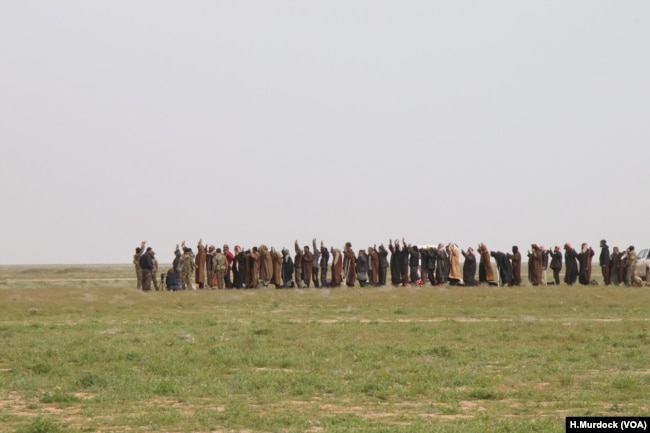 Men line up to be searched and then investigated for suspected connections to the Islamic State group after leaving the battle for IS's last stronghold, which is not much more than a camp along the banks of the Euphrates River, Feb. 26, 2019. (H.Murdock/VOA)