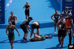 Mexico's Cecilia Perez, center, collapses after competing in a women's triathlon test event at Odaiba Marine Park, a venue for marathon swimming and triathlon at the Tokyo 2020 Olympics, Thursday, Aug. 15, 2019, in Tokyo. Olympic officials say they are concerned about high temperatures in Tokyo during the Games.