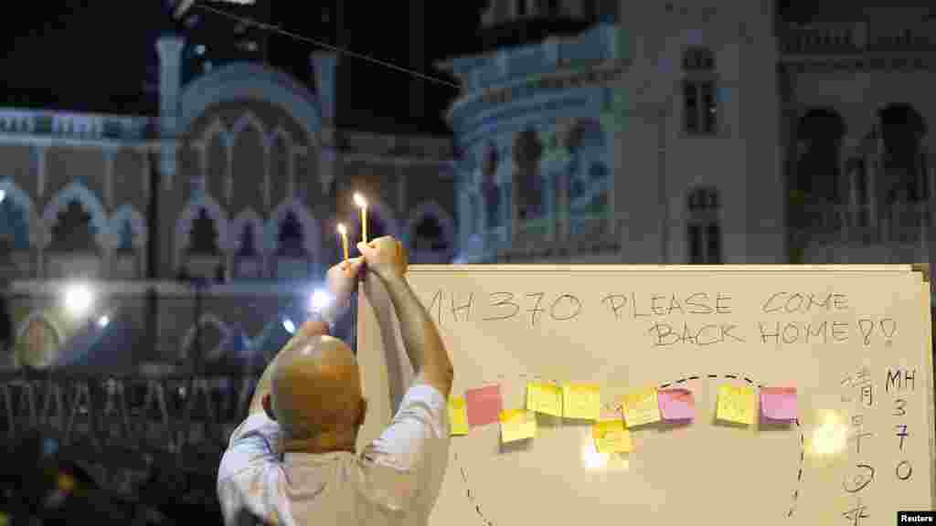 A man places a candle on top of a white board set up to place messages for passengers on Flight MH370 during a candlelight vigil in Kuala Lumpur, April 6, 2014. 