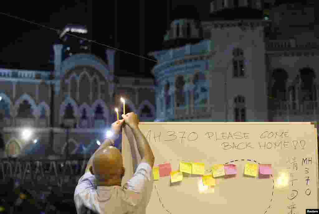 A man places a candle on top of a white board set up to place messages for passengers on Flight MH370 during a candlelight vigil in Kuala Lumpur, April 6, 2014. 