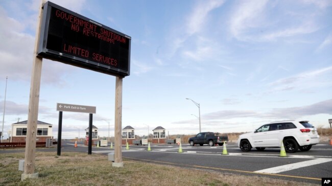 FILE - Vehicles roll into the Gateway National Recreation Area-Sandy Hook near a sign at the entrance warning visitors of limited services such as closed restrooms during the partial government shutdown in Highlands, N.J., Jan. 3, 2019.