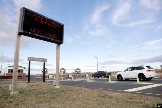 FILE - Vehicles roll into the Gateway National Recreation Area-Sandy Hook near a sign at the entrance warning visitors of limited services such as closed restrooms during the partial government shutdown in Highlands, N.J., Jan. 3, 2019.