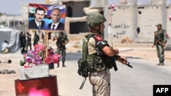 FILE - Members of Russian and Syrian forces stand guard near posters of Syrian President Bashar al-Assad and his Russian counterpart, Vladimir Putin, at the Abu Duhur crossing on the eastern edge of Idlib province, Syria, Aug. 20, 2018.