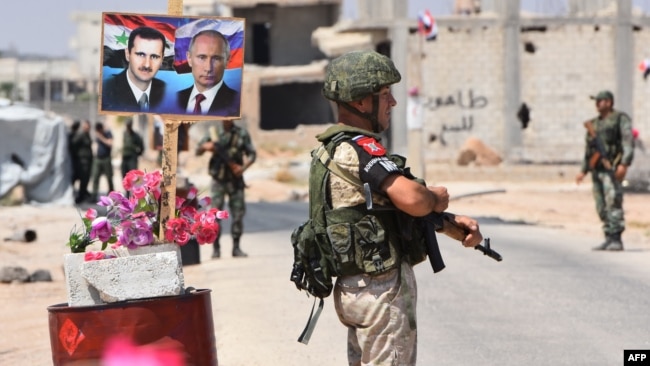 Members of Russian and Syrian forces stand guard near posters of Syrian President Bashar al-Assad and his Russian counterpart Vladimir Putin at the Abu Duhur crossing on the eastern edge of Idlib province, Aug. 20, 2018.