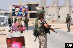 FILE - Members of Russian and Syrian forces stand guard near posters of Syrian President Bashar al-Assad and his Russian counterpart, Vladimir Putin, at the Abu Duhur crossing on the eastern edge of Idlib province, Aug. 20, 2018.