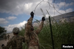 Con el muro fronterizo detrás, en Hidalgo, Texas, militares estadounidenses colocan una barrera de alambre de púas. Nov. 9 de 2018.