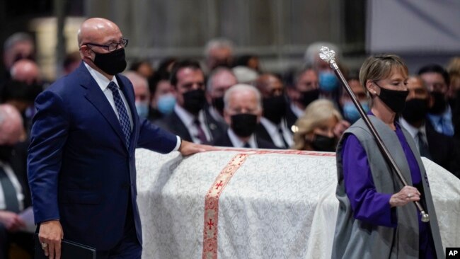 Michael Powell touches the casket of his father, former Secretary of State Colin Powell, as he walks to give a eulogy during a funeral service at the Washington National Cathedral, Nov. 5, 2021, in Washington. President Joe Biden looks on.