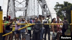 FILE - People stand next to a closed gate as they wait to try to cross La Union international bridge, on the border with Colombia at Boca de Grita in Tachira state, Venezuela, Aug. 29, 2015. 