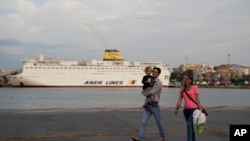 A couple with their child walk in front of a docked ferry at the port of Piraeus near Athens, May 16, 2017. 