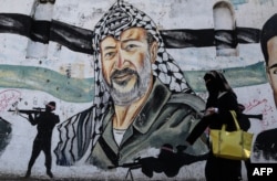 A veiled Palestinian woman walks past a mural on a wall depicting late Palestinian leader Yasser Arafat as Palestinians mark the 14th anniversary of Arafat's death, in Gaza City, Nov. 11, 2018.
