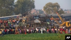 People gather as rescuers work the scene after 14 cars of an overnight passenger train rolled off the track near Pukhrayan village Kanpur Dehat district, Uttar Pradesh state, India, Nov. 20, 2016.