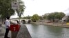 A journalist poses in front of a bright red, eco-friendly urinal on the Ile Saint-Louis along the Seine River in Paris, France, Aug. 13, 2018. 