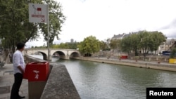 A journalist poses in front of a bright red, eco-friendly urinal on the Ile Saint-Louis along the Seine River in Paris, France, Aug. 13, 2018. 