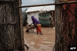 FILE - A woman cooks on a wheelbarrow beside flooded shelters after a heavy rainy season downpour at the Dadaab refugee complex, in the north-east of Kenya, on April 17, 2018.