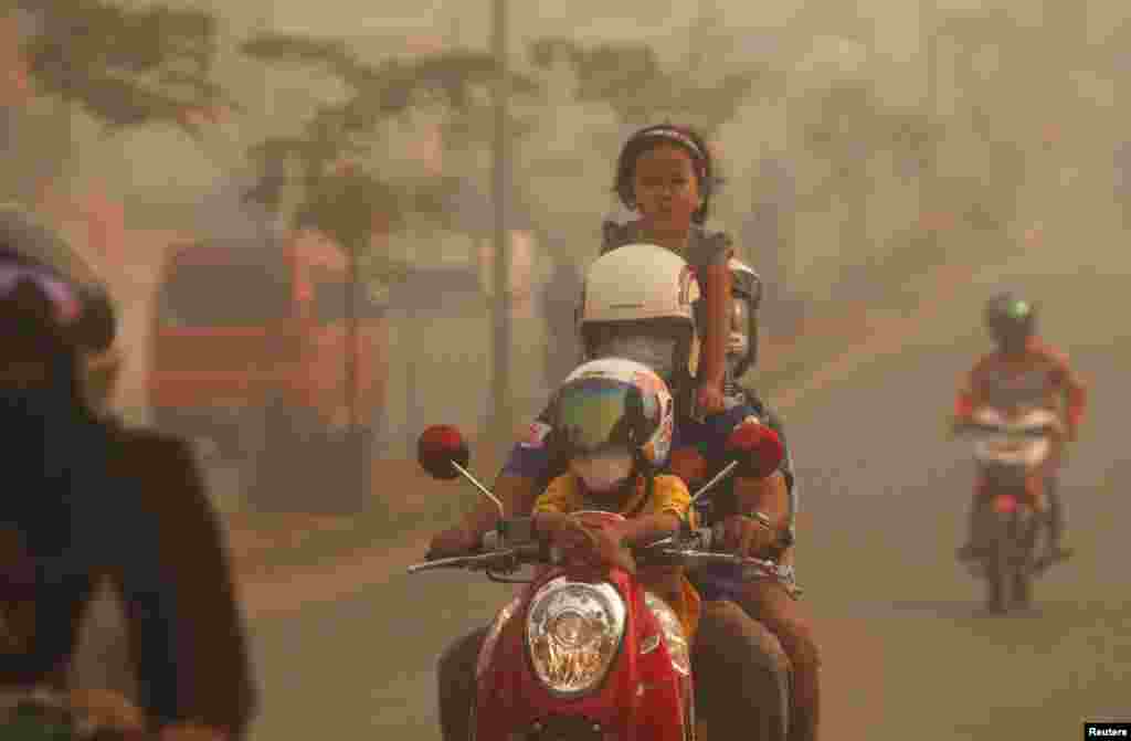A family rides on a motorcycle in the haze which hit Duri on Indonesia&#39;s Riau province. Indonesian police arrested two farmers for illegally starting fires to clear land in Sumatra - the first detentions linked to blazes that have blanketed neighboring Singapore and Malaysia with thick smog for days.