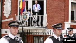 Ông Assange đứng trên bao lơn đại sứ quán Ecuador ở London. Ông Assange được Ecuador cho phép tỵ nạn, nhưng chính phủ Anh không cho ông rời London vì Anh có nghĩa vụ giải giao ông cho Thụy Điển, nơi đã có trát bắt ông