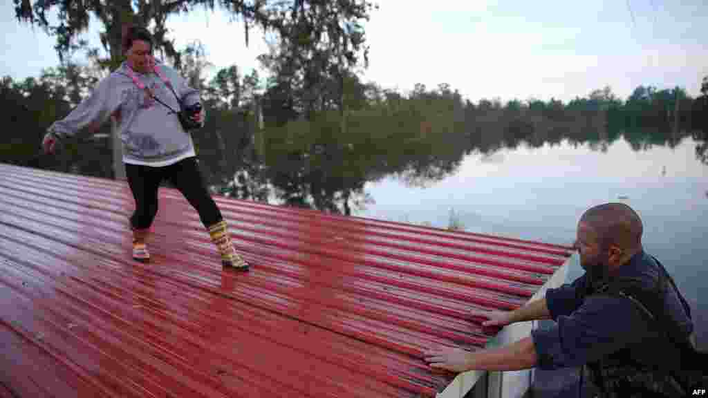 Seorang perempuan AS di kota&nbsp;​Andrews, South Carolina melewati atap rumah akibat banjir, sementara suaminya menunggu di atas sebuah perahu.