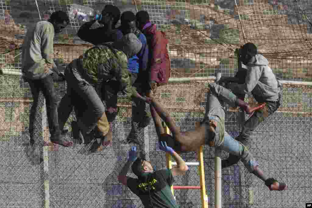 A sub-Saharan migrant is helped by a Spanish Guardia Civil officer after he fainted on top of a metallic fence that divides Morocco and the Spanish enclave of Melilla. Spanish and Moroccan police have thwarted a fresh attempt by dozens of African migrants to try to scale border fences to enter the Spanish enclave of Melilla.