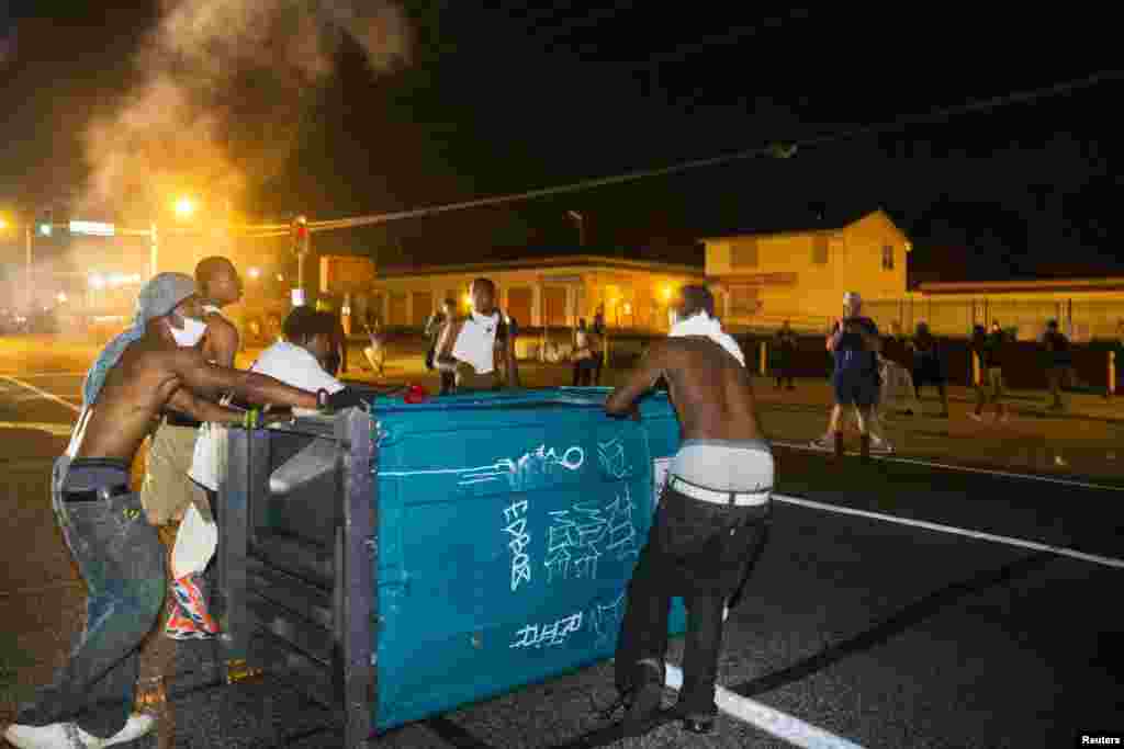 Demonstrators drag a portable toilet onto the roadway during protests in Ferguson, Missouri August 18, 2014.