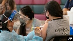 FILE - Sisters Guadalupe Flores, 15, right, and Estela Flores, 13, left, from East Los Angeles, get vaccinated with the Pfizer's COVID-19 vaccine at the Esteban E. Torres High School in Los Angeles, May 27, 2021. (AP Photo/Damian Dovarganes)