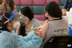 Sisters Guadalupe Flores, 15, right, and Estela Flores, 13, left, from East Los Angeles, get vaccinated with the Pfizer's COVID-19 vaccine by licensed vocational nurse Rita Orozco, far left, at the Esteban E. Torres High School in Los Angeles, Thursday, M