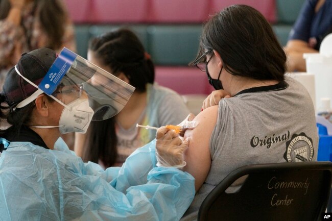 Sisters Guadalupe Flores, 15, right, and Estela Flores, 13, left, from East Los Angeles, get vaccinated with the Pfizer's COVID-19 vaccine by licensed vocational nurse Rita Orozco, far left, at the Esteban E. Torres High School in Los Angeles, Thursday, M