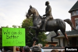 FILE - Protesters gather below a monument dedicated to Confederate Major John B. Castleman while demanding that it be removed from the public square in Louisville, Kentucky, Aug. 14, 2017.