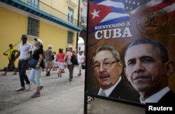 Tourists pass by images of U.S. President Barack Obama and Cuban President