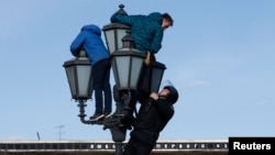 A riot police officer climbs on a lamp pole to detain opposition supporters during a rally in Moscow, Russia, March 26, 2017.