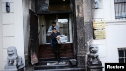 Workers carry stacks of newspaper from the steps of the fire-damaged front of the Chinese consulate in San Francisco, California, Jan. 2, 2014.