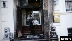 Workers carry stacks of newspaper from the steps of the damaged front of the Chinese consulate a fire at the main gate in San Francisco, California January 2, 2014.