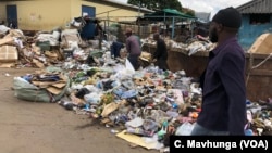 FILE: Some Harare citizens walk by a heap of waste which has not been collected for days. Experts say that is a breeding zone for cholera.