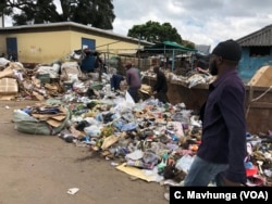 Some Harare citizens walk by a heap of waste which has not been collected for days. Experts say that is a breeding zone for cholera.