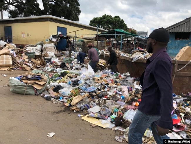 Some Harare citizens walk by a heap of waste which has not been collected for days. Experts say that is a breeding zone for cholera.