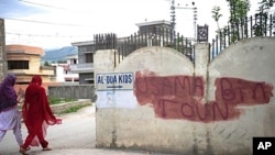 Pakistani women walk past covered graffiti that reads "Usama bin Laden toun" (Osama bin Laden town) in Abbottabad on May 6, 2011, where bin Laden was killed by US commandos in a secret raid on May 2.