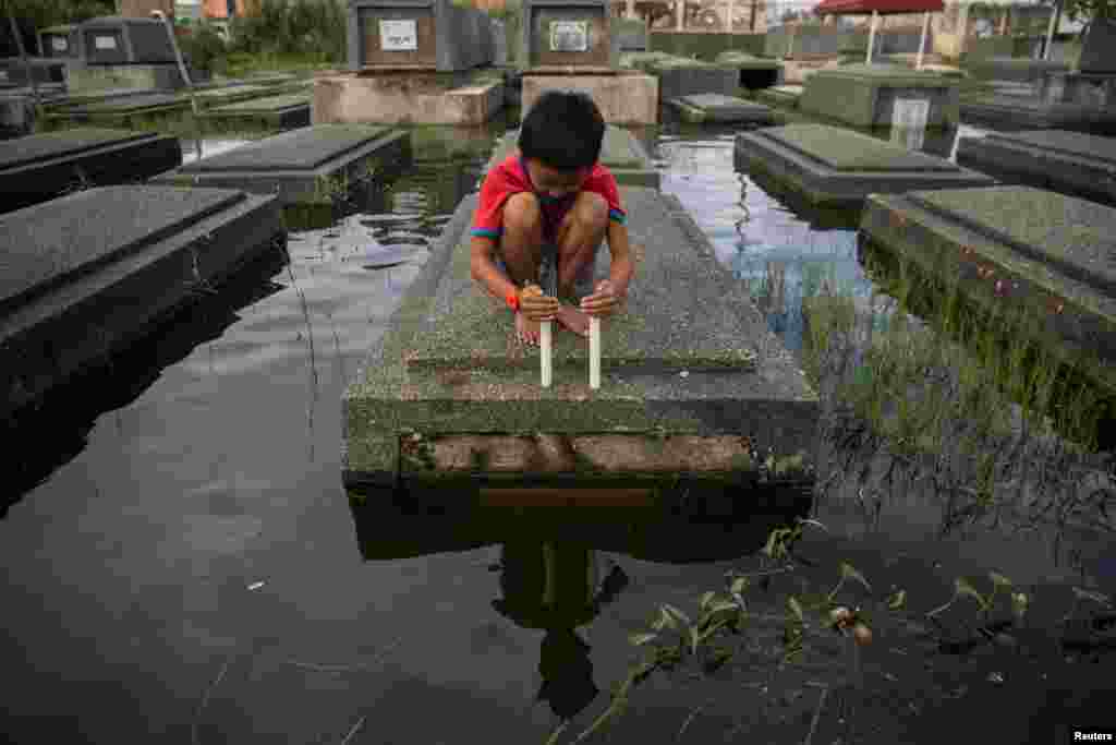 A boy attempts to keep a candle lit in a flooded cemetery following Typhoon Molave, in Masantol, Pampanga, Philippines.