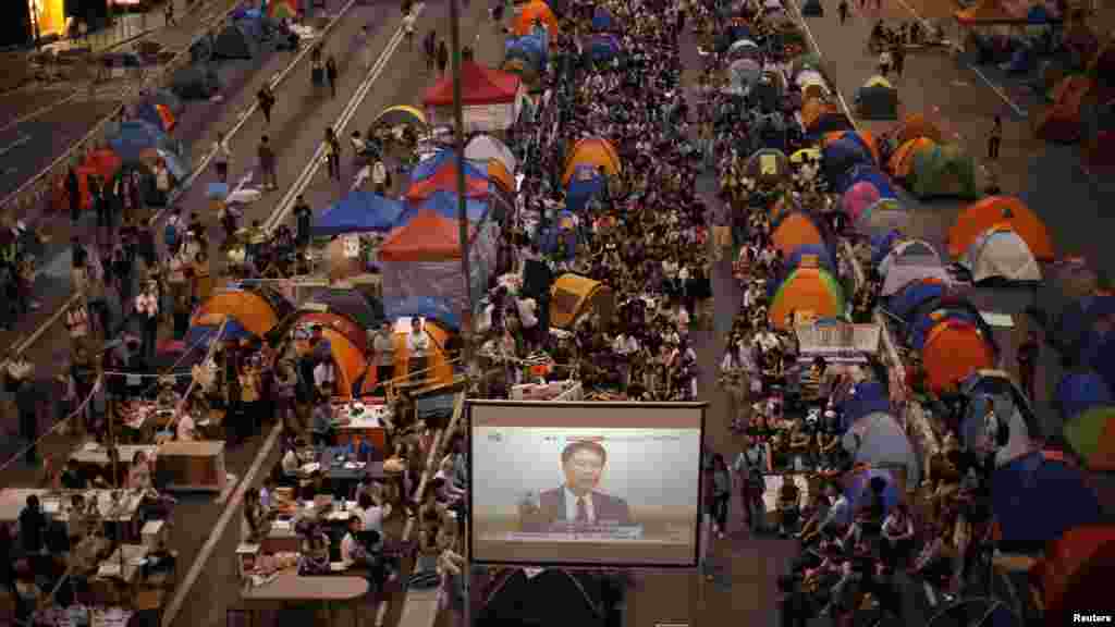 Para demonstran pro-demokrasi menonton pembicaraan formal antara para pemimpin protes mahasiswa dan pejabat pemerintah dari layar video dekat kantor pusat pemerintahan di Hong Kong (21/10). (Reuters/Carlos Barria) 