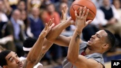 FILE - Reggie Moore, right, playing for Washington State at the time, shoots over Pittsburgh's Cameron Wright, left, during a College Basketball Invitational tournament best-of-three championship, March 28, 2012, in Pittsburgh, Pennsylvania. Moore now plays in Angola's professional league.